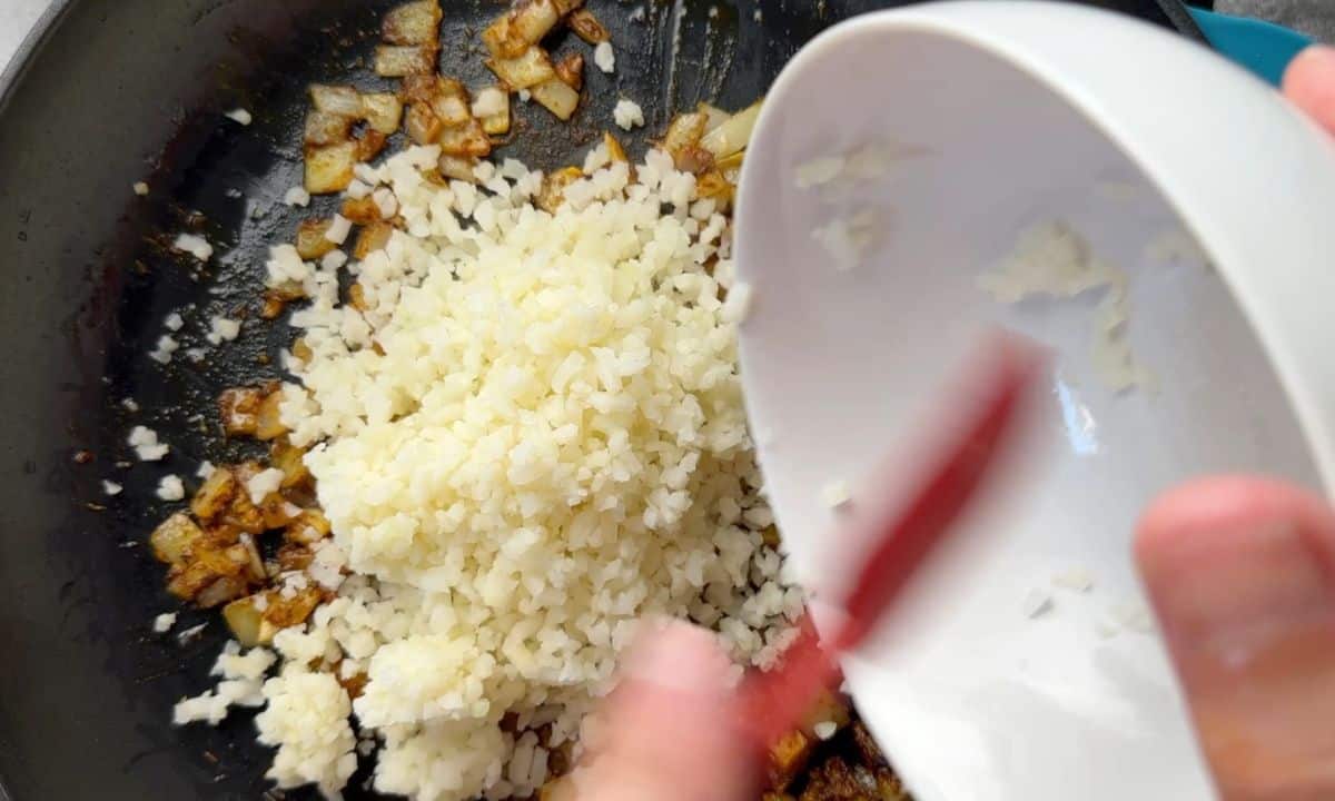 Adding cauliflower rice in the skillet.