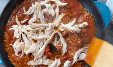 Shredded chicken on top of the sauce and cauliflower rice in the skillet.