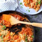 Low carb tex mex chicken and cauliflower rice in a skillet with a wooden spoon next to a plateful of the recipe dish.