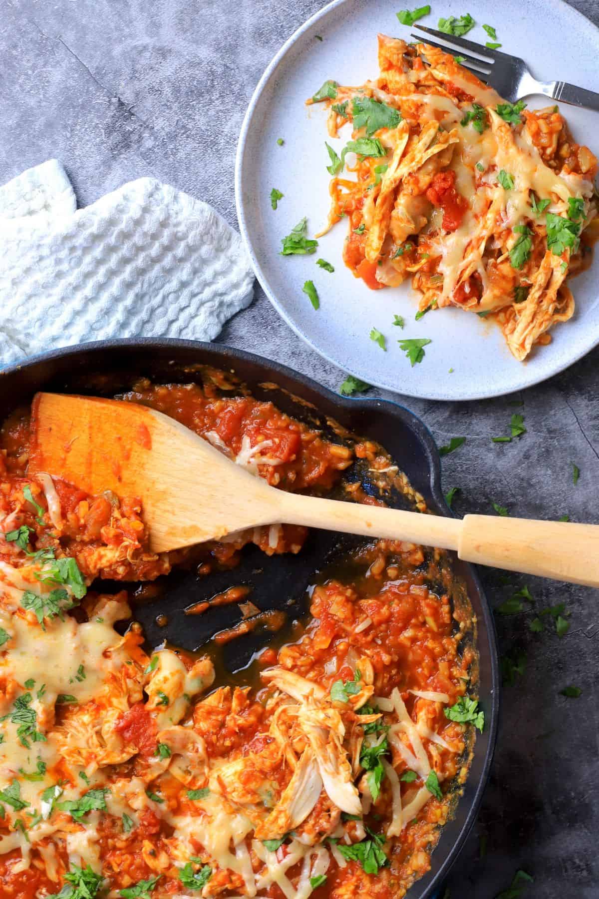 Low carb tex mex chicken and cauliflower rice in a skillet with a wooden spoon next to a plate with the same.