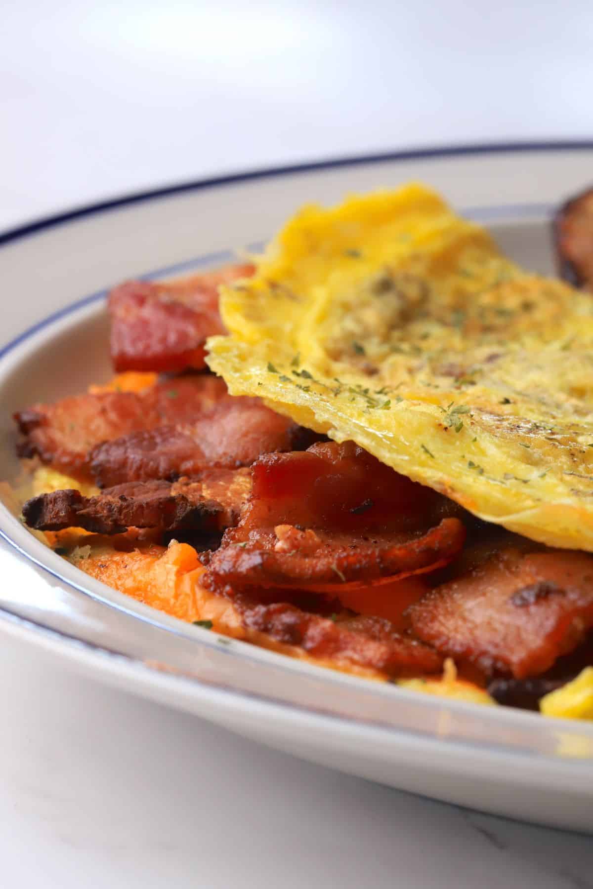Omelet stuffed with bacon and cheddar on a plate.