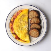 Omelet stuffed with bacon and cheddar on a plate with breakfast sausage patties.