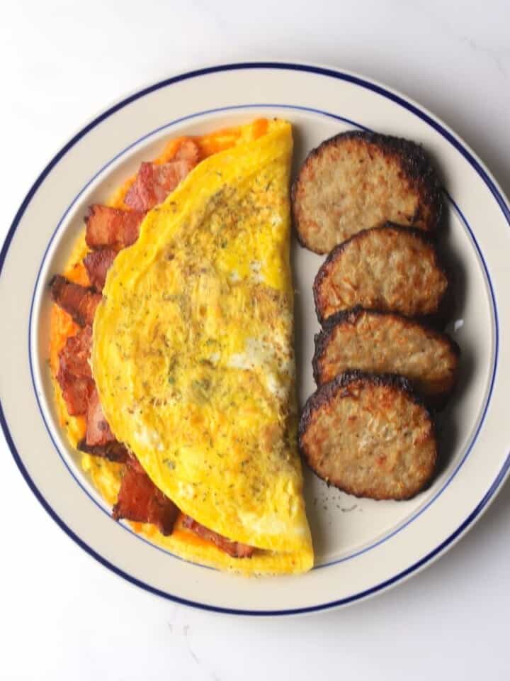 Omelet stuffed with bacon and cheddar on a plate with breakfast sausage patties.