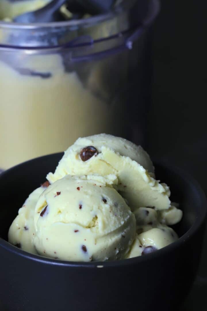 Black bowl with scoops of sugar free mint chocolate chip ice cream with the ninja creami pint in the background.