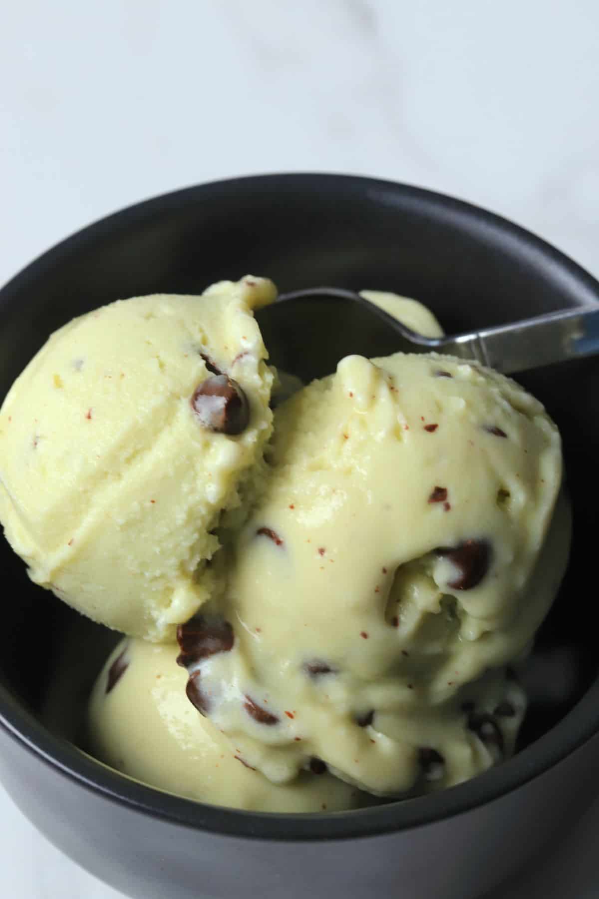Black bowl with scoops of sugar free mint chocolate chip ice cream.