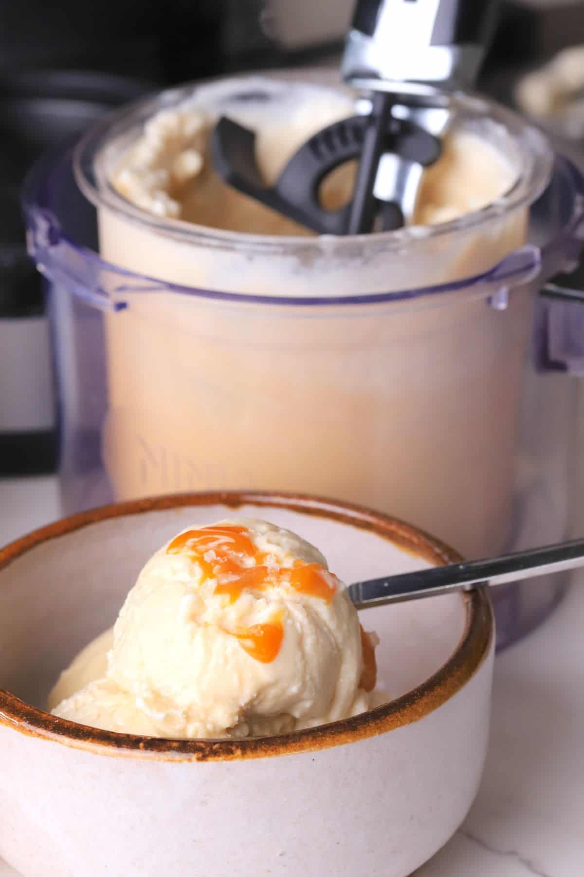 Sugar free salted caramel ice cream in a bowl next to a creami pint with an ice cream scoop.