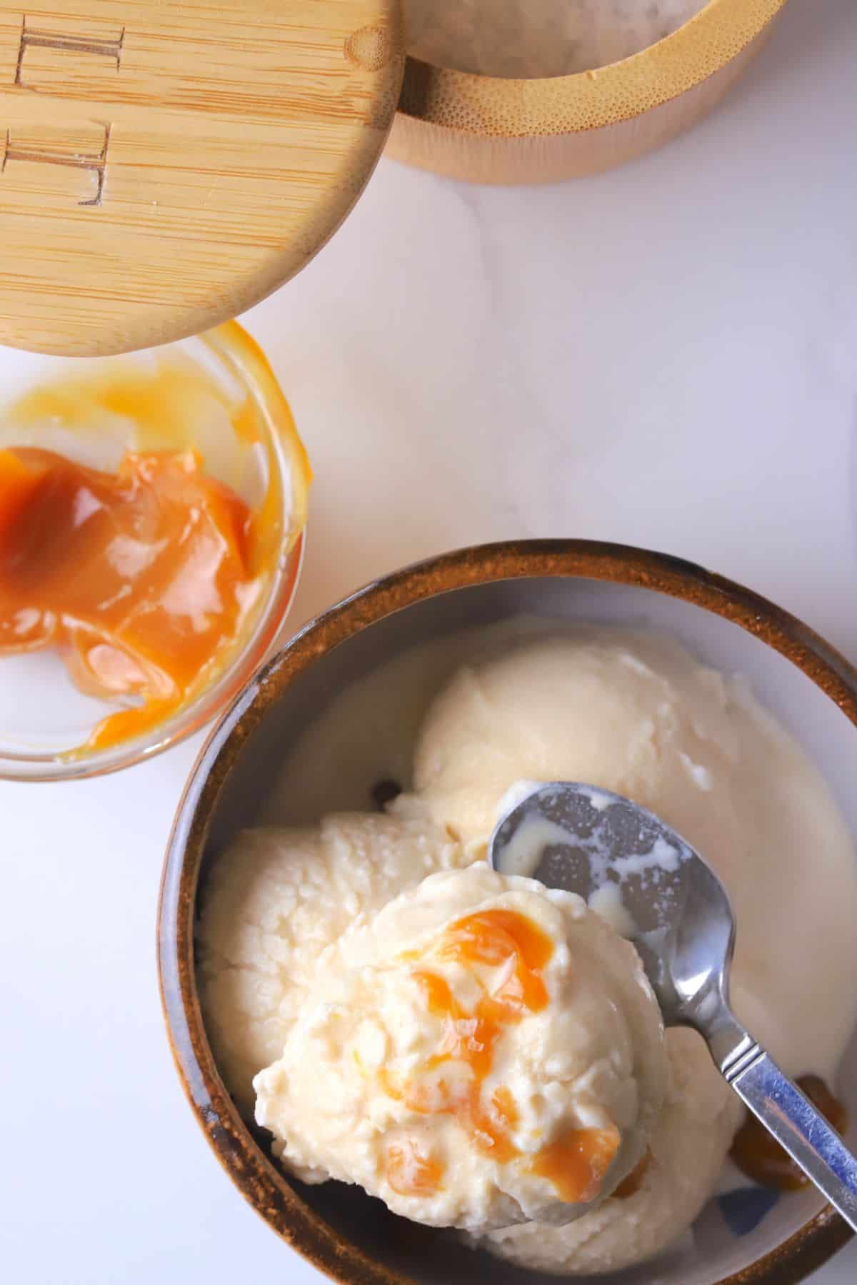 Sugar free salted caramel ice cream in a bowl next to a small bowl of caramel and a salt container.
