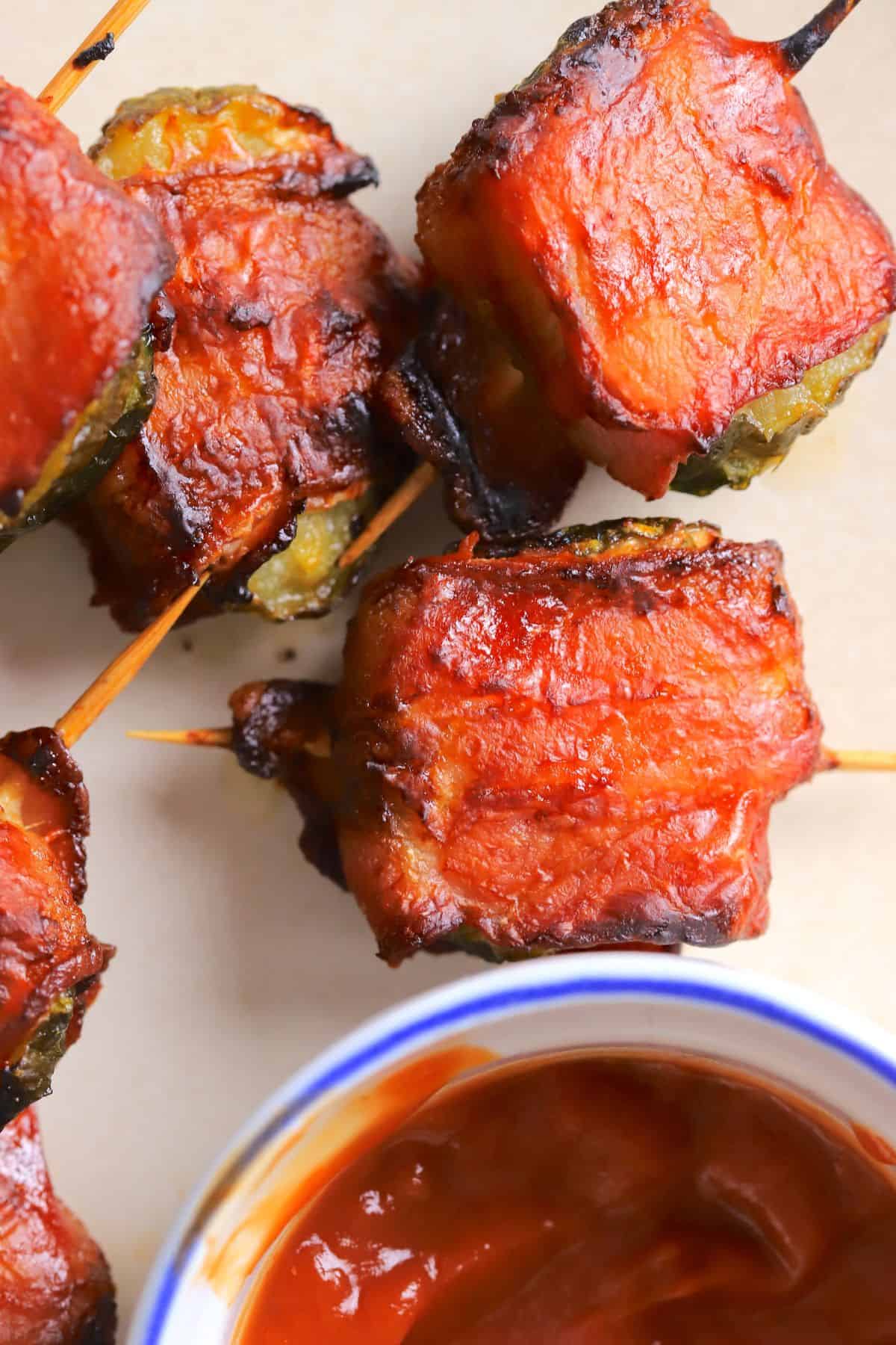 A plate with bacon wrapped pickles next to a side of ketchup.