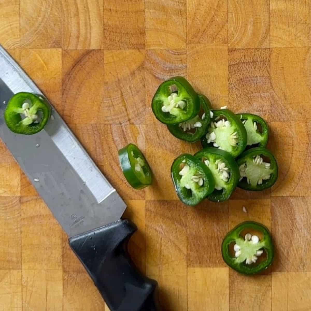 Slices of jalapenos on a cutting board with a knife.