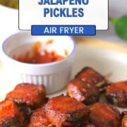 A plate with bacon wrapped pickles next to a side of ketchup, pickle slices, toothpicks and a jalapeno.