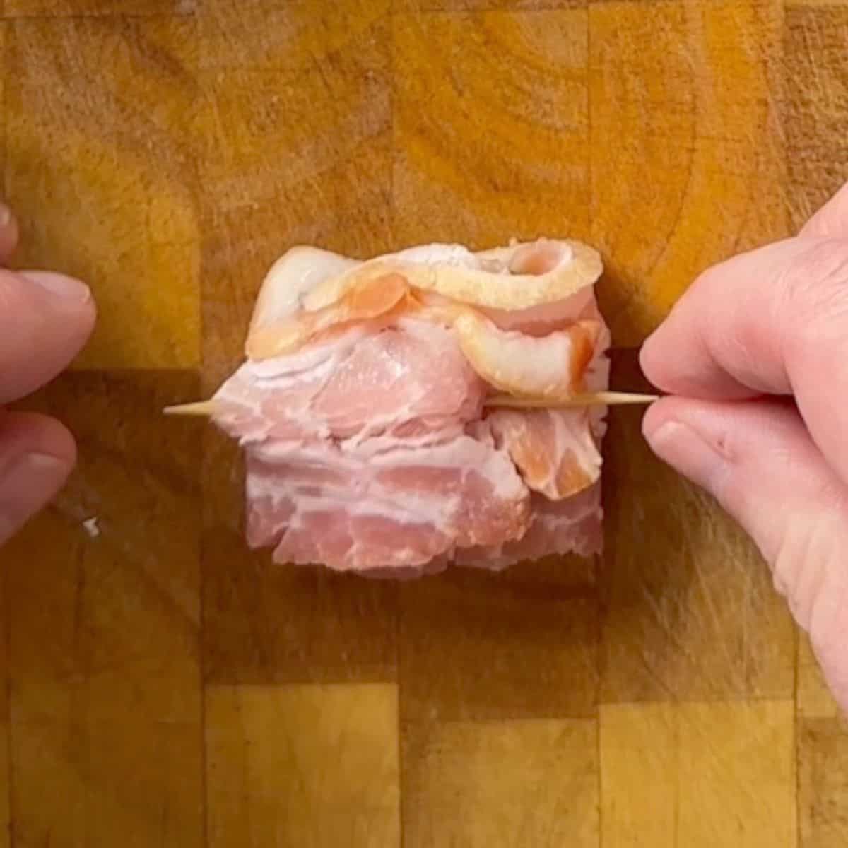 Threading a toothpick through an uncooked bacon wrapped pickle.