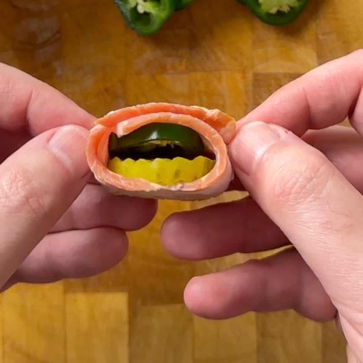 An uncooked bacon wrapped jalapeno pickle.