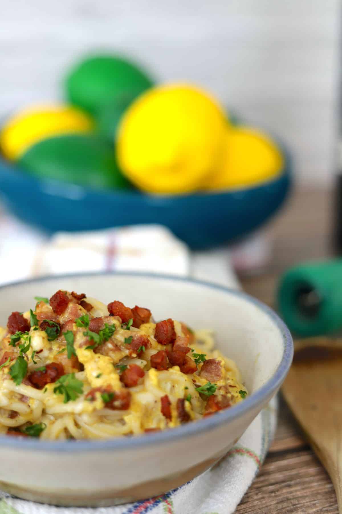 Bowl full of dairy free spaghetti carbonara topped with chopped parsley and pancetta.