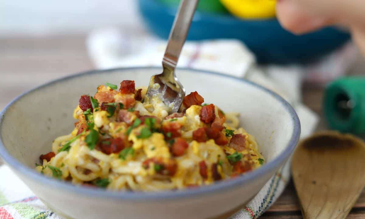 Bowl full of dairy free spaghetti carbonara topped with chopped parsley and pancetta.