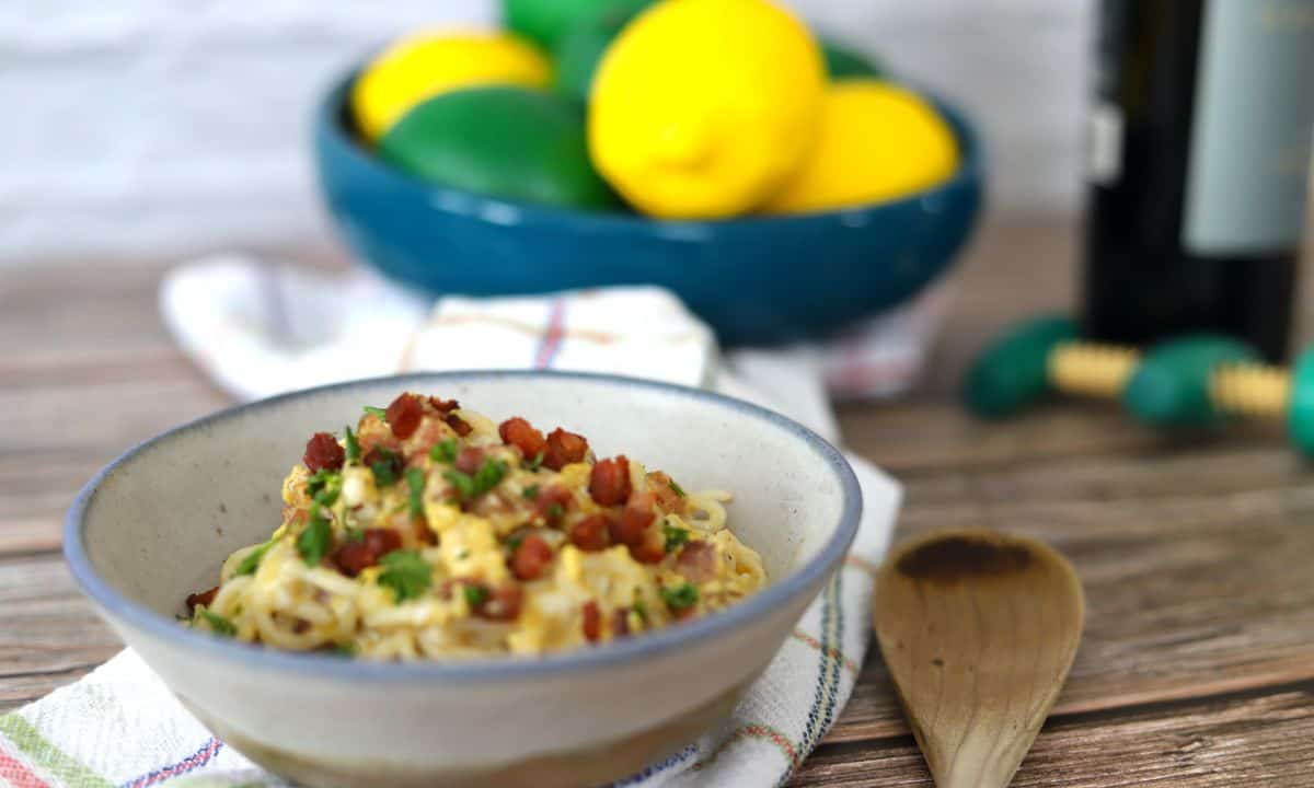 Bowl full of dairy free spaghetti carbonara topped with chopped parsley and pancetta.