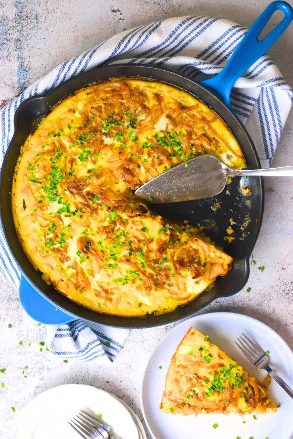 A slice of low carb french onion frittata on a plate next to the skillet.