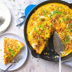 A slice of low carb french onion frittata on a plate next to the skillet.