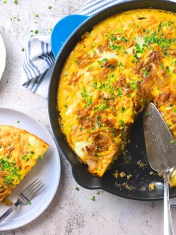 A slice of low carb french onion frittata on a plate next to the skillet.