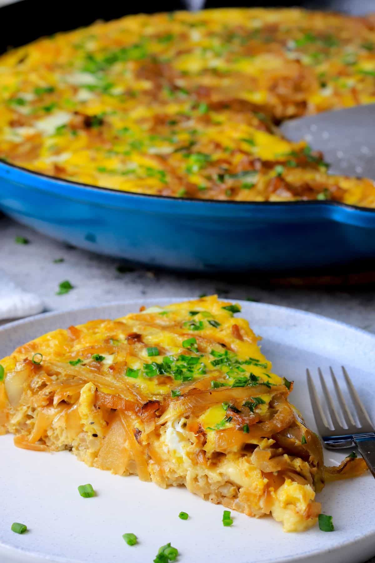 A slice of low carb french onion frittata on a plate next to the skillet.