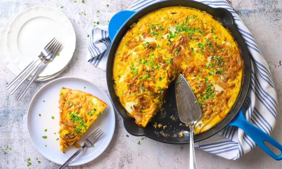 A slice of low carb french onion frittata on a plate next to the skillet.