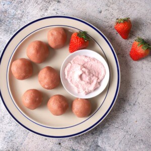 Strawberry protein bliss balls on a plate with a side of strawberry cream dip and fresh strawberries.