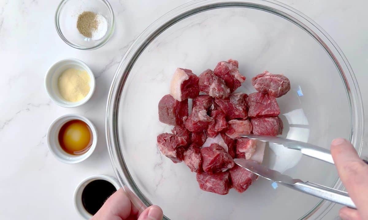 Cubed steak in a large bowl next to ingredients in small bowls.