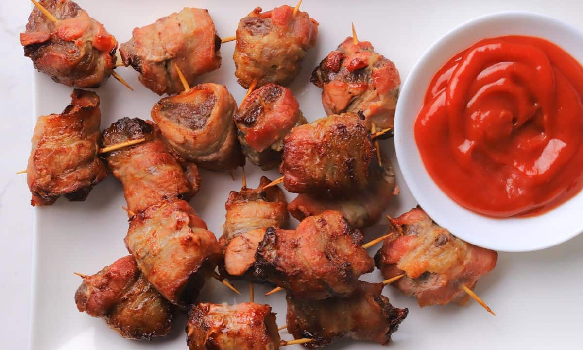 Bacon wrapped steak bites on a platter with a side dish of ketchup.