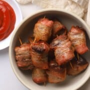 Bacon wrapped steak bites in a bowl with a side dish of ketchup.