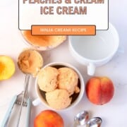 Bowl full of peach ice cream next to a peach, ice cream scoop and some spoons.