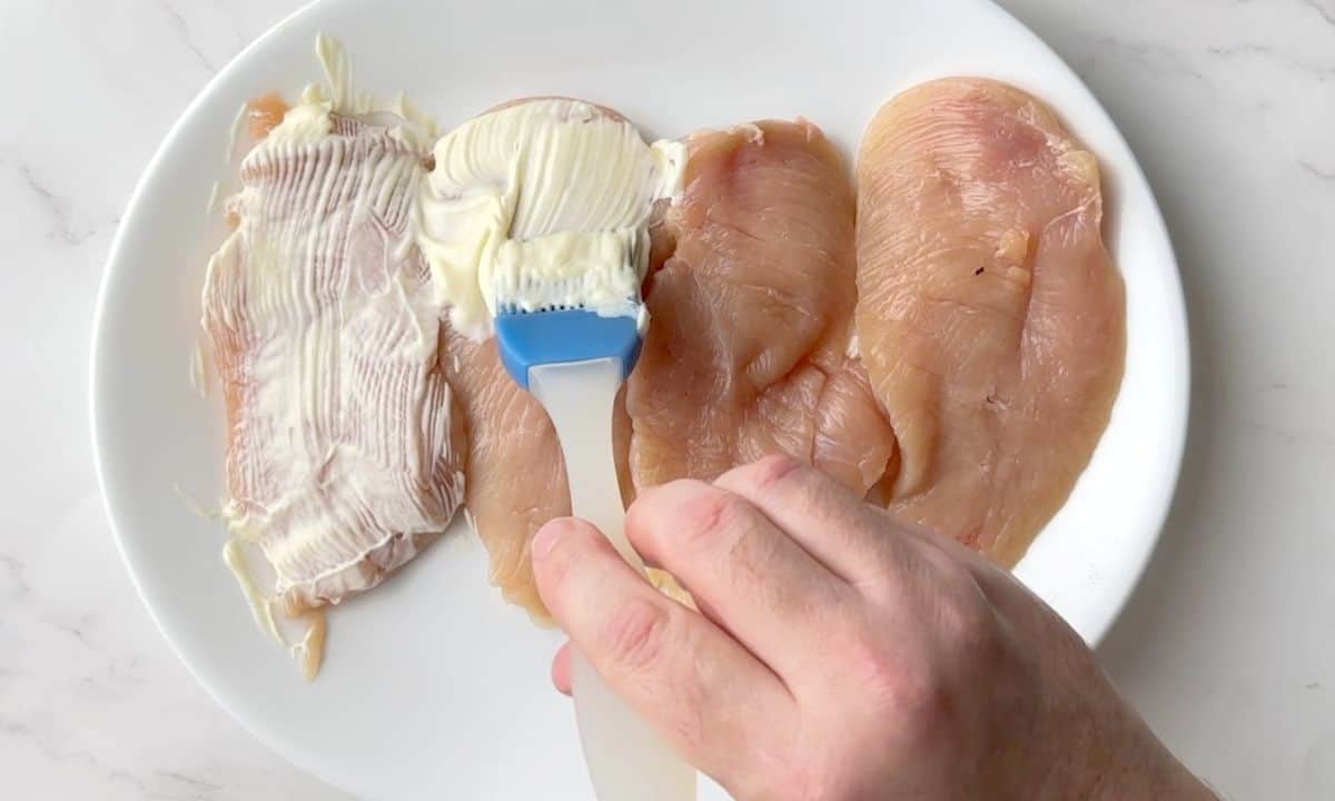 Brushing chicken breast with mayonnaise.