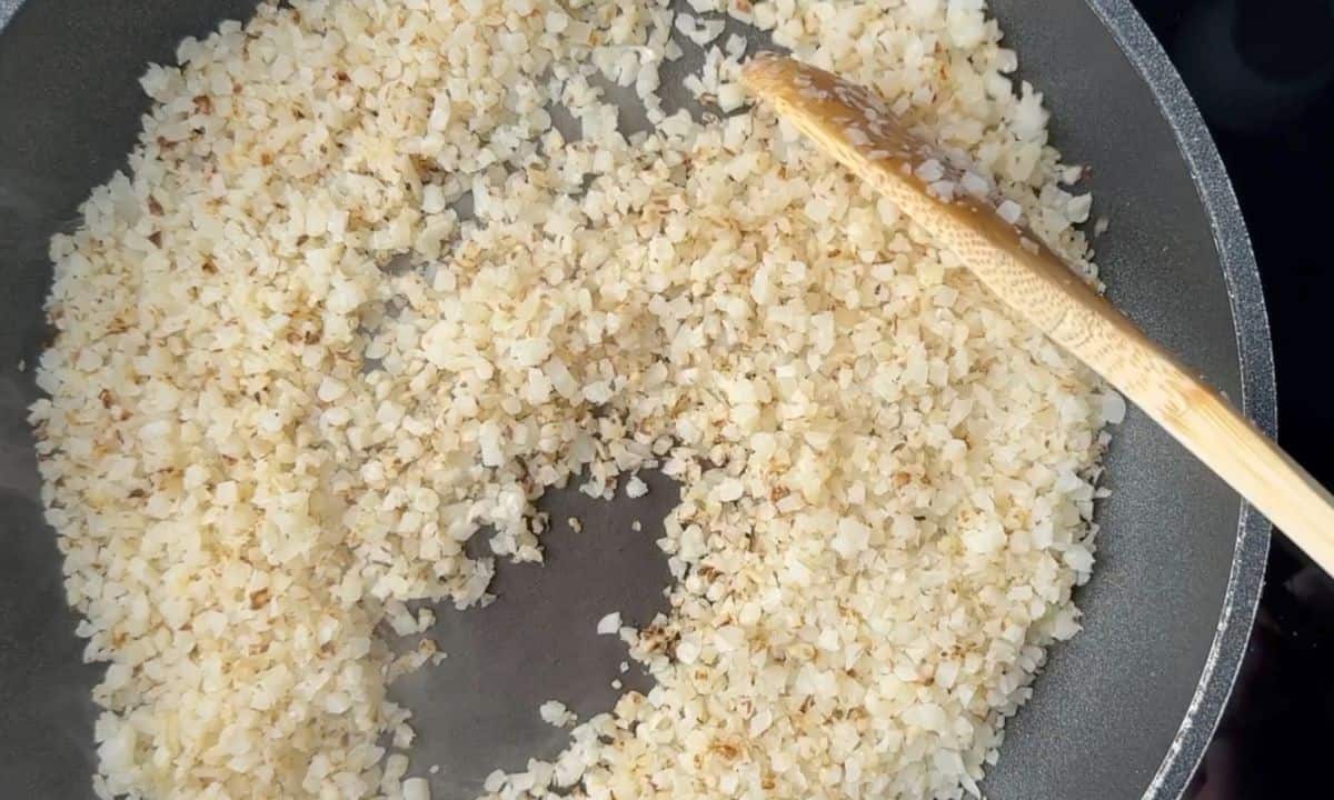 Cauliflower rice frying in a pan.