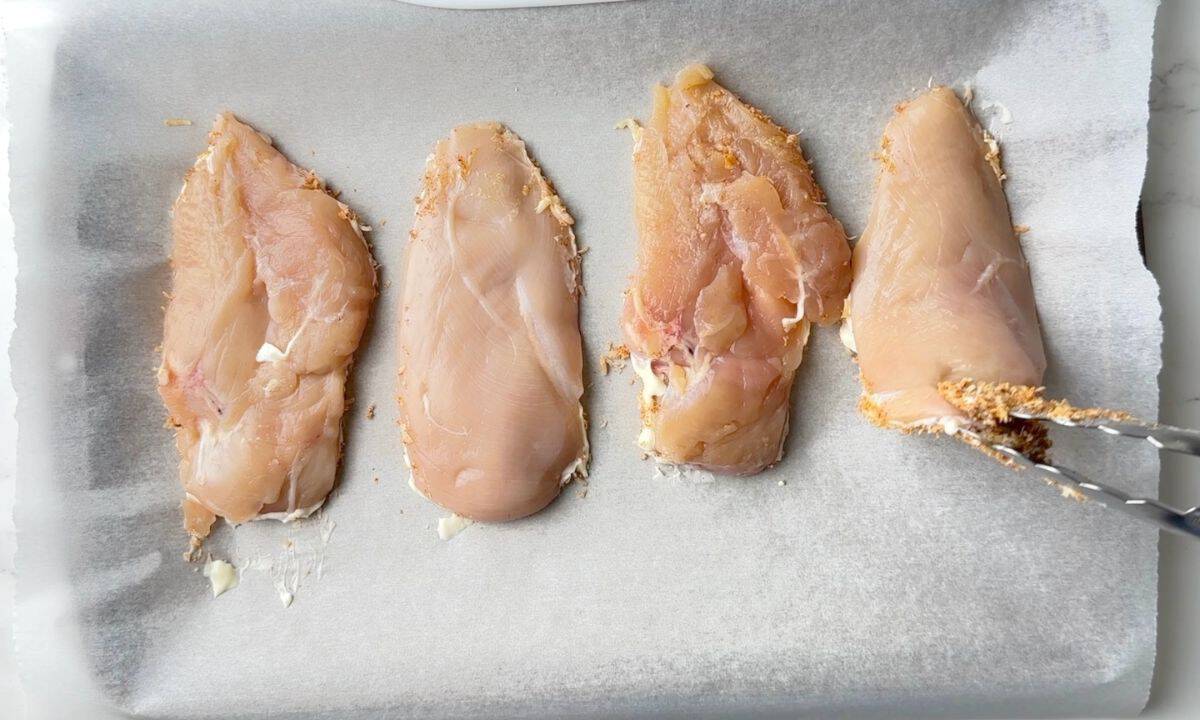 Chicken breasts on a parchment lined backing sheet.
