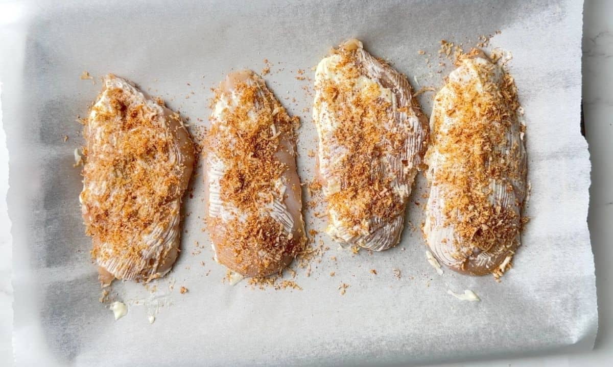 Chicken on a parchment lined sheet pan brushed with mayonnaise and the parmesan mixture.
