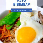 A white bowl filled with a bibimbap recipe of crispy cauliflower rice, beef, shredded carrots, snow peas and topped with a fried egg.