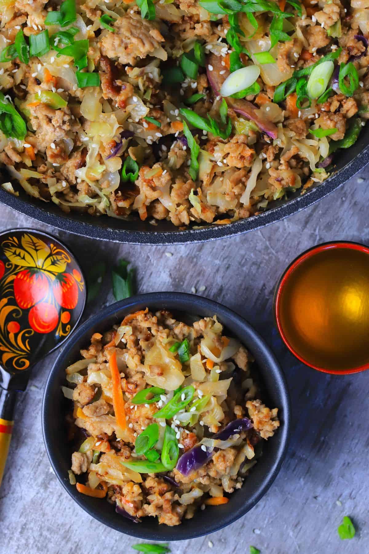 Low carb thai eggroll in a bowl in a large bowl next to a spoon, a cup and a pan with the same.