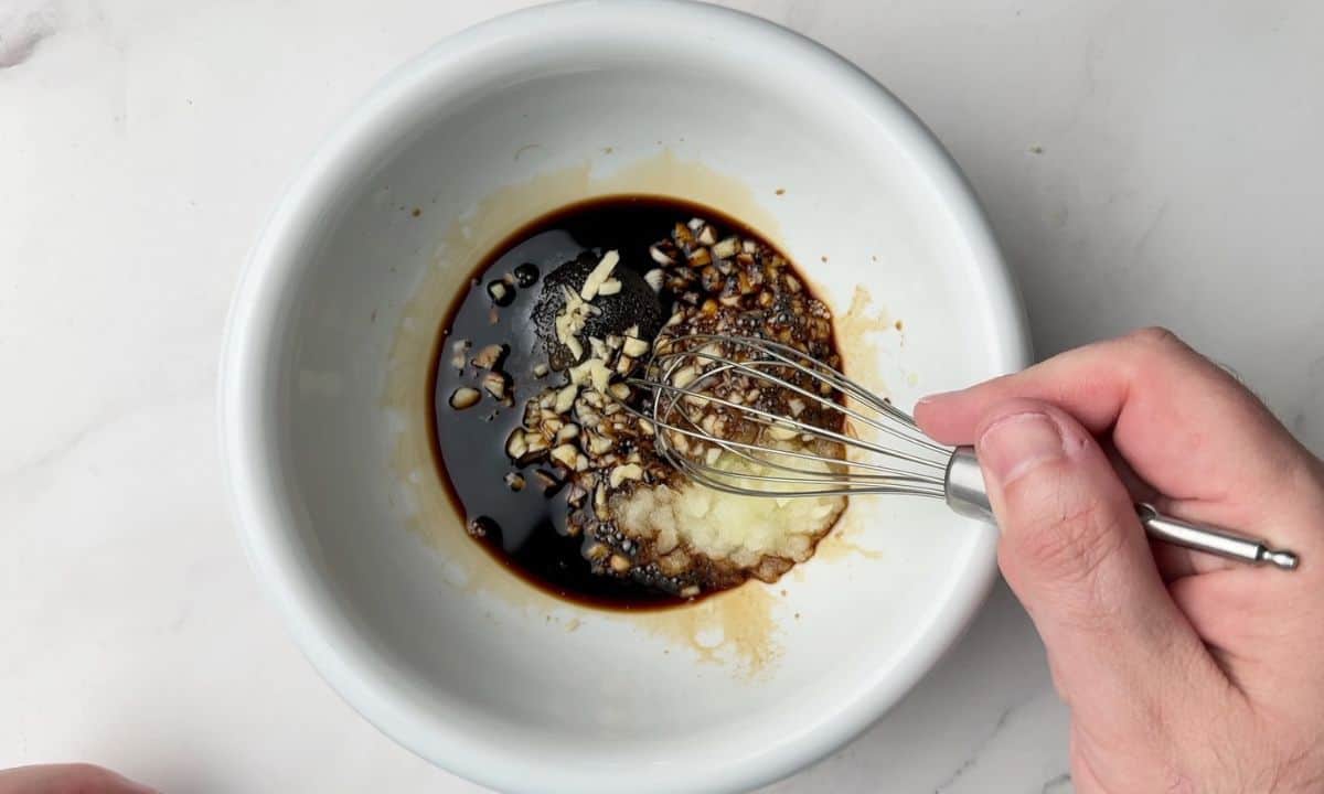 Whisking the marinade for the recipe in a large white bowl.