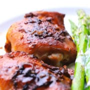 Two sticky chicken thighs with a low carb sauce on a plate next to asparagus spears.