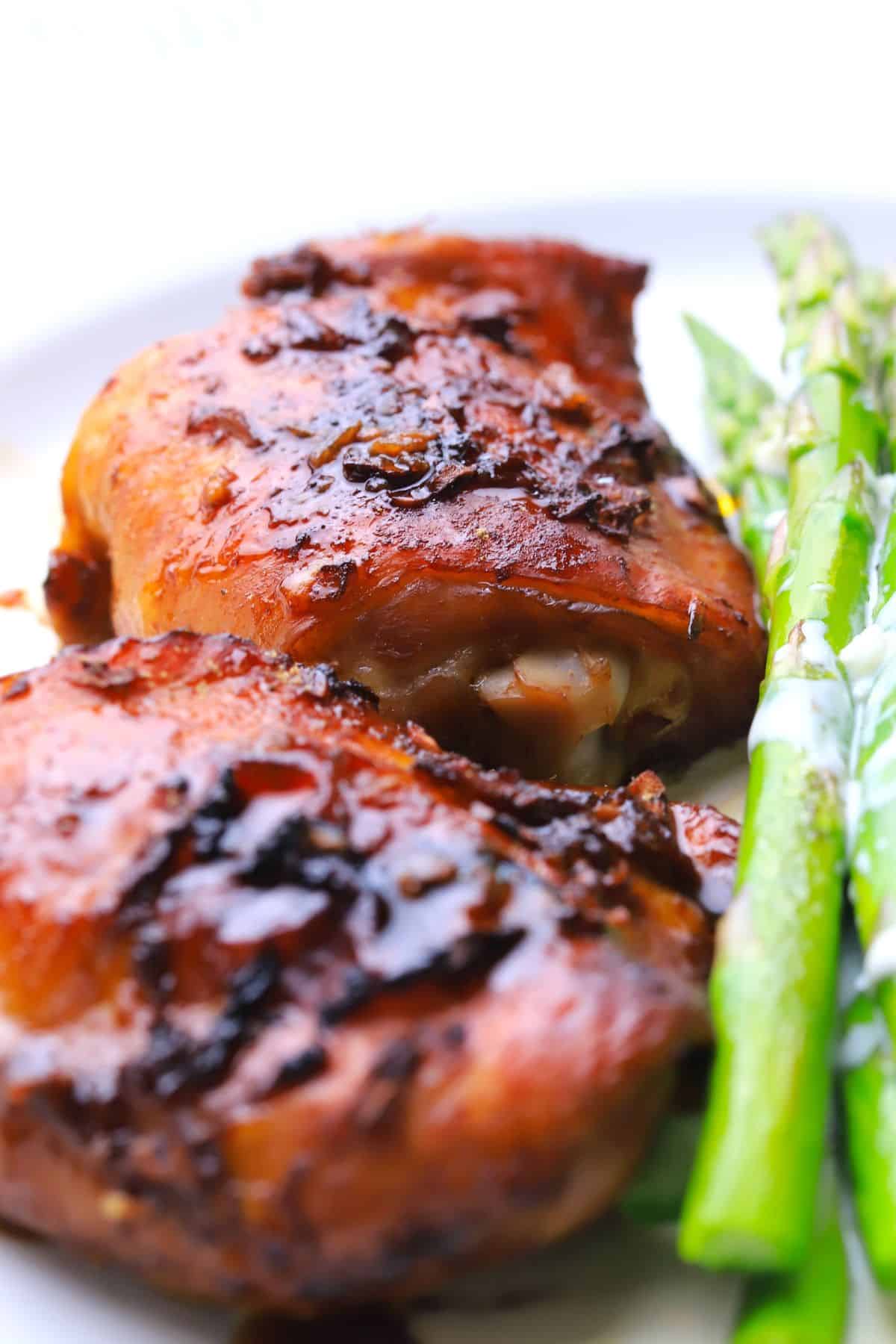 Two sticky chicken thighs with a low carb sauce on a plate next to asparagus spears.