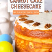 Sugar free carrot cake decorated with cream cheese frosting next to a coffee mug, a ceramic bunny rabbit and colored easter eggs.