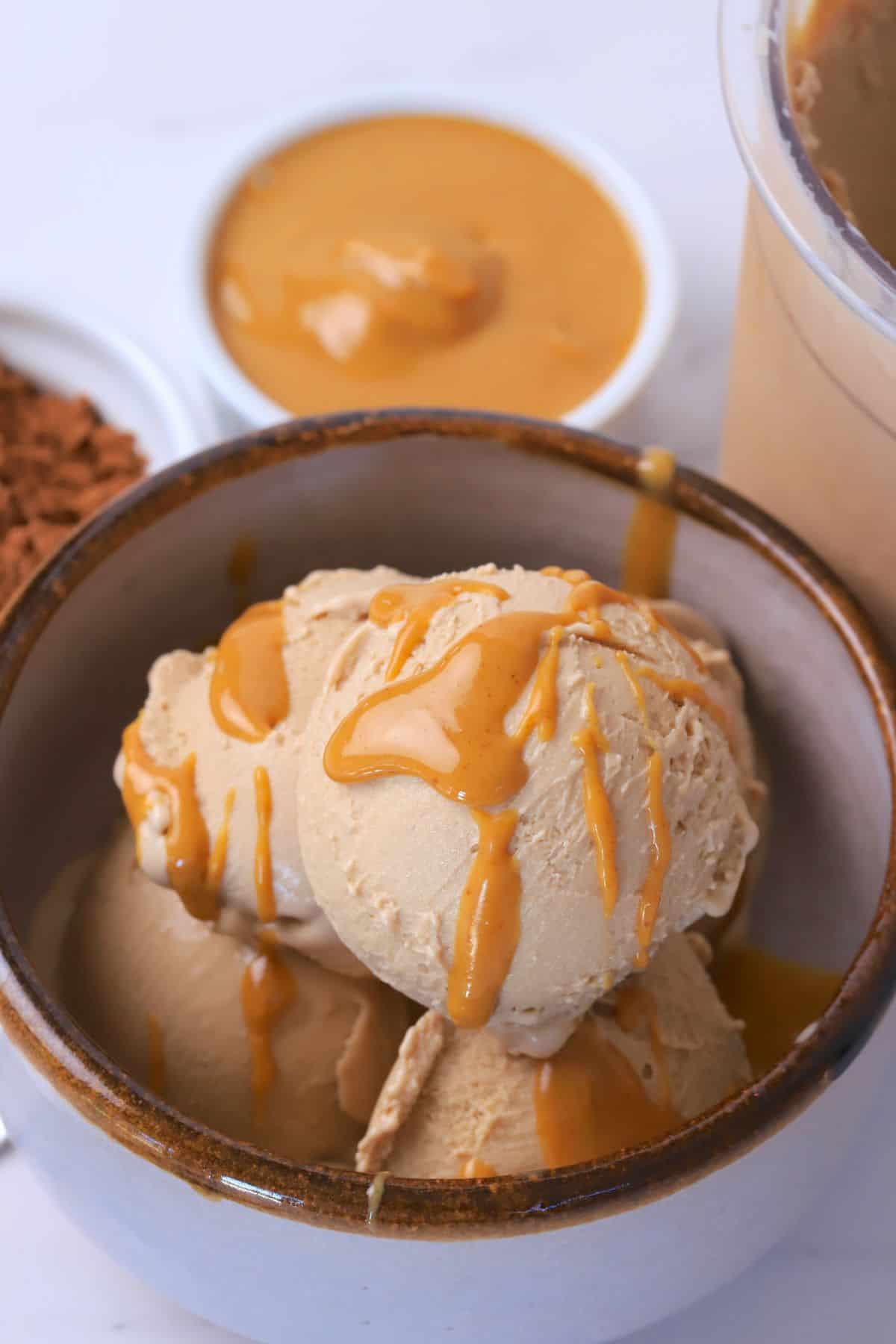 Sugar free chocolate peanut butter ice cream in a bowl topped with a drizzle of peanut butter with a small bowls of chocolate protein powder and a small bowl of creamy peanut butter.
