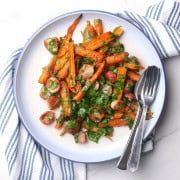 The herbed carrots and radishes on a white plate with a fork and spoon.