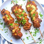 Low bang bang chicken skewers on a plate drizzled with bang bang sauce and garnished with chopped cilantro.