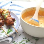 Low bang bang chicken skewers on a plate drizzled with bang bang sauce and garnished with chopped cilantro. Bowl on the side with more bang bang sauce.