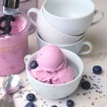 Blueberry lavender ice cream in a white bowl with blueberries and the ninja creami pint in the background.