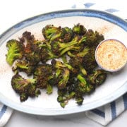 Burnt broccoli on a white plate with a side bowl of dip.