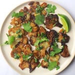Smashed cauliflower on a plate topped with cilantro and a side wedge of a lime.