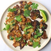 Smashed cauliflower on a plate topped with cilantro and a side wedge of a lime.