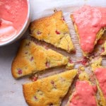 Low carb raspberry scones half are iced on a parchment lined baking sheet next to a bowl with more icing.