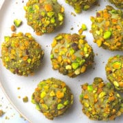 Low carb pistachio balls on a plate with crushed pistachios around them.