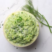 Creamy Mashed Broccoli and Cauliflower in a bowl topped with chopped chives and grated parmesan, with a sprig of dill on the side.